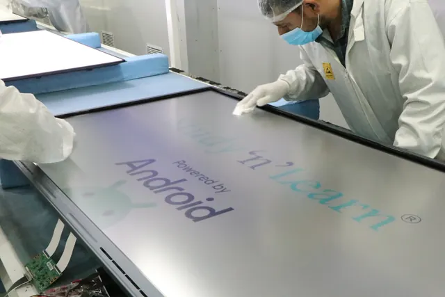Technician in gloves and a face mask wiping the screen of an interactive panel on the assembly bench