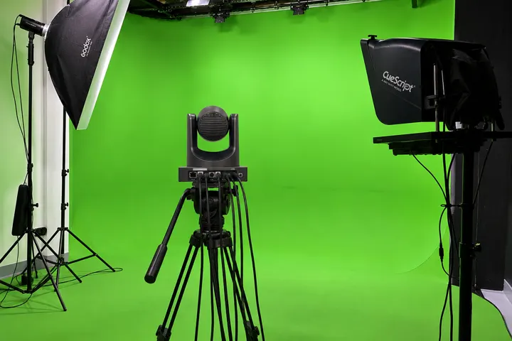 Presenter standing in front of a green screen backdrop with studio lighting and an overhead PTZ camera
